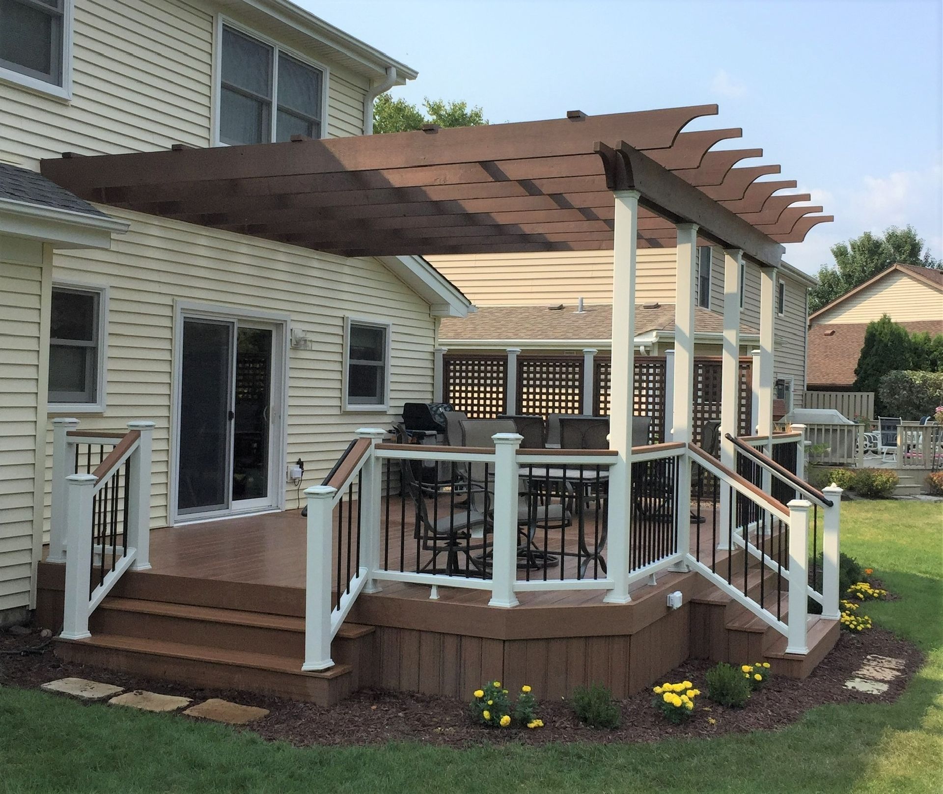 Backyard deck with pergola, railing, and outdoor dining set beside a beige house
