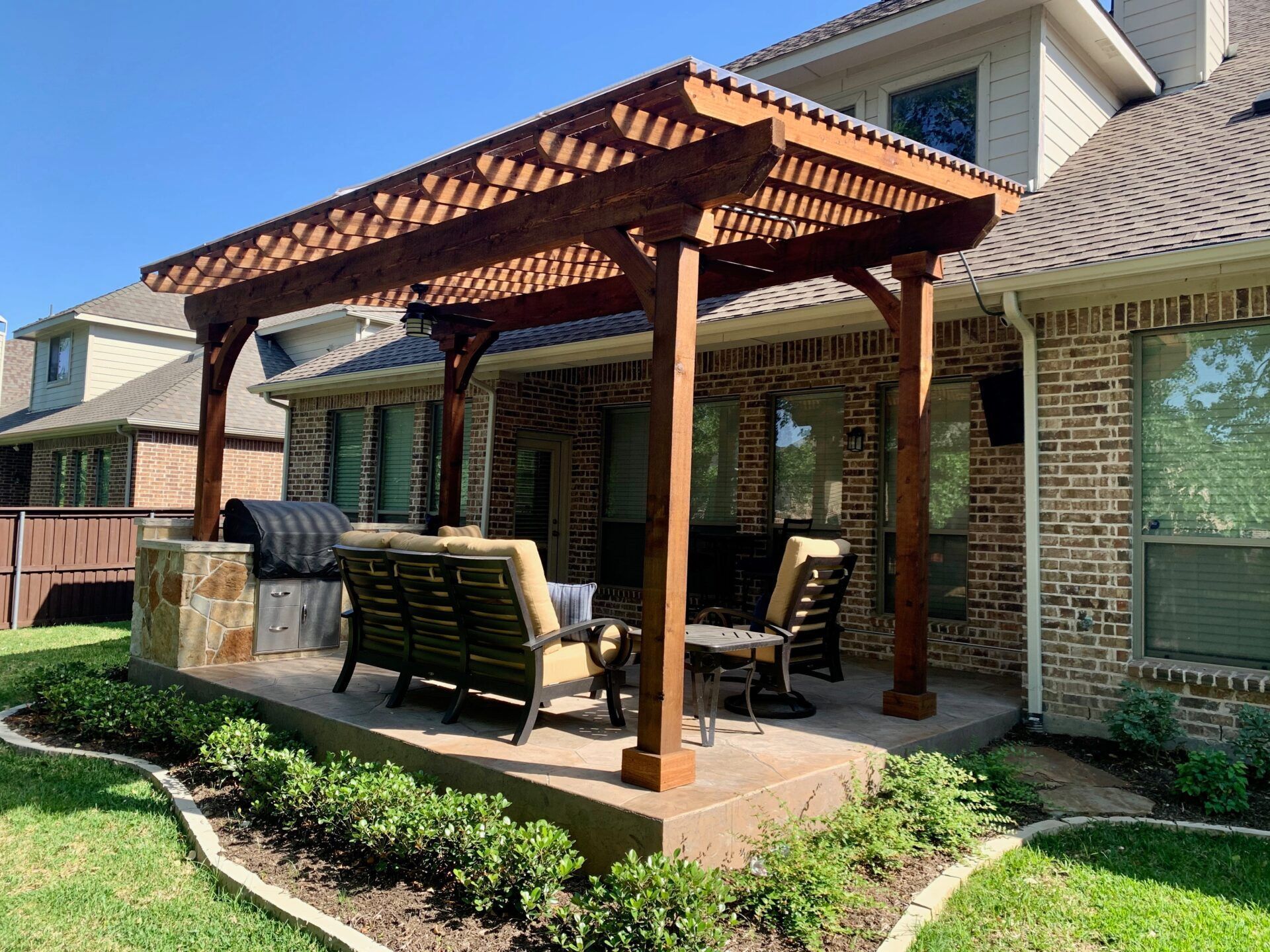 Backyard patio with wooden pergola, outdoor dining set, grill, and brick house exterior