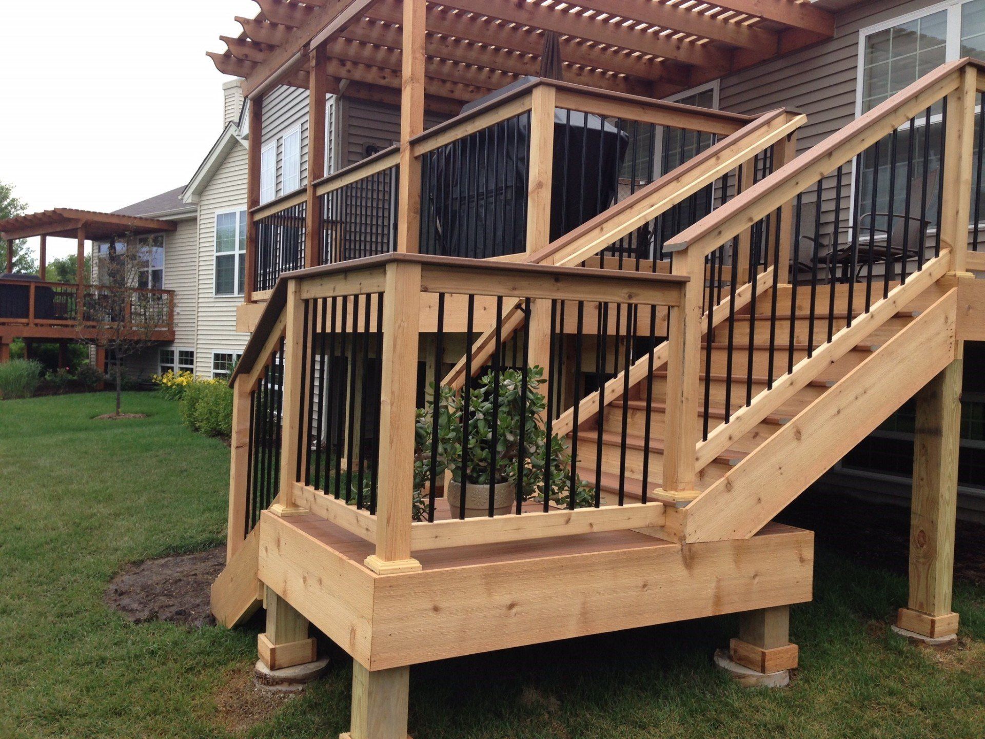 Wooden deck stairs and railing beside a house, with a small lower porch and grassy yard.