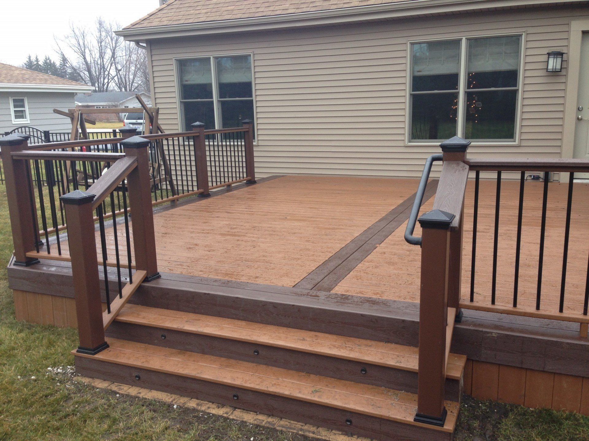 Wooden backyard deck with railing and steps leading to a beige house.