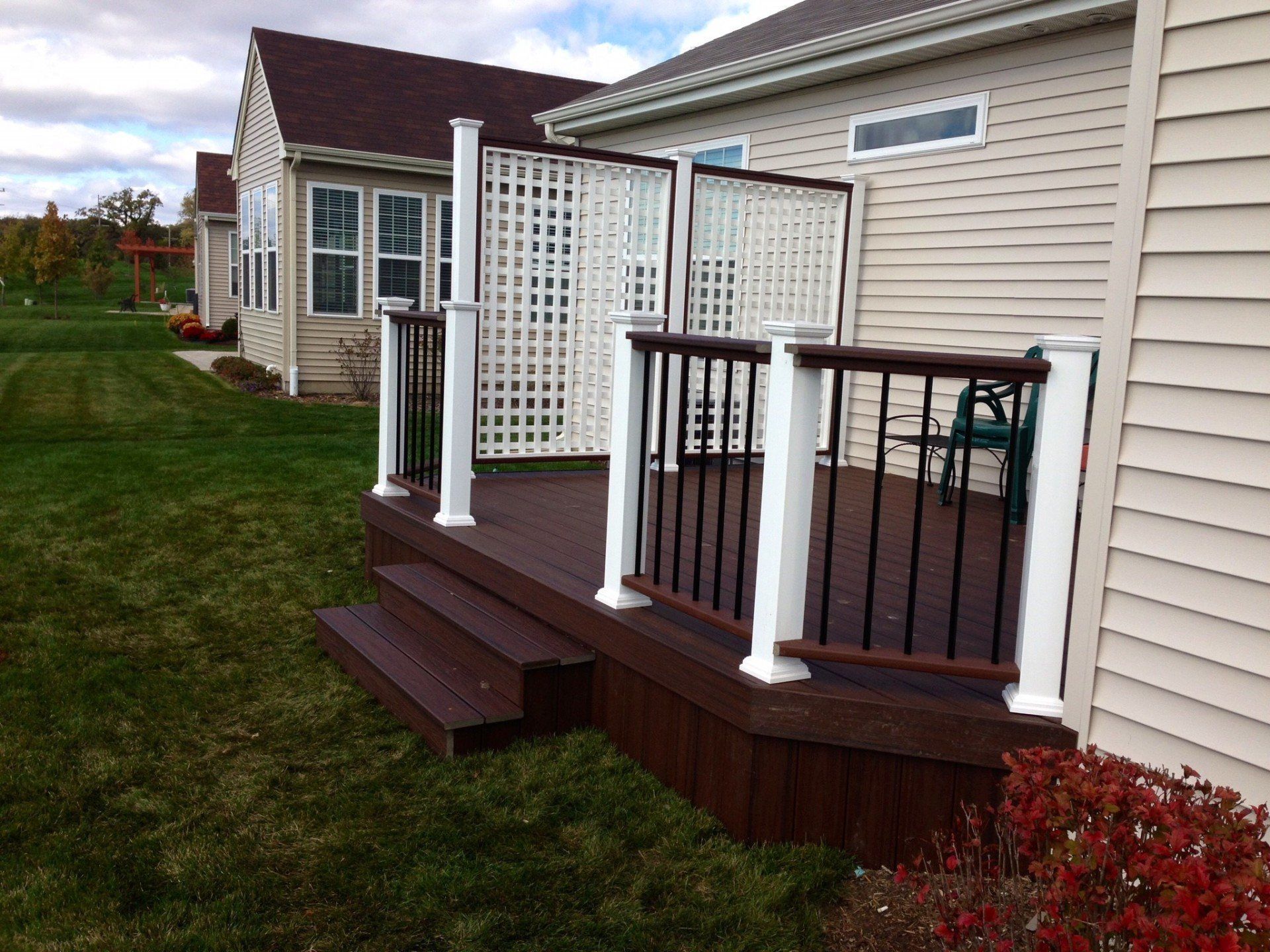 Back deck with white lattice railing, brown steps, and beige house siding in a suburban yard