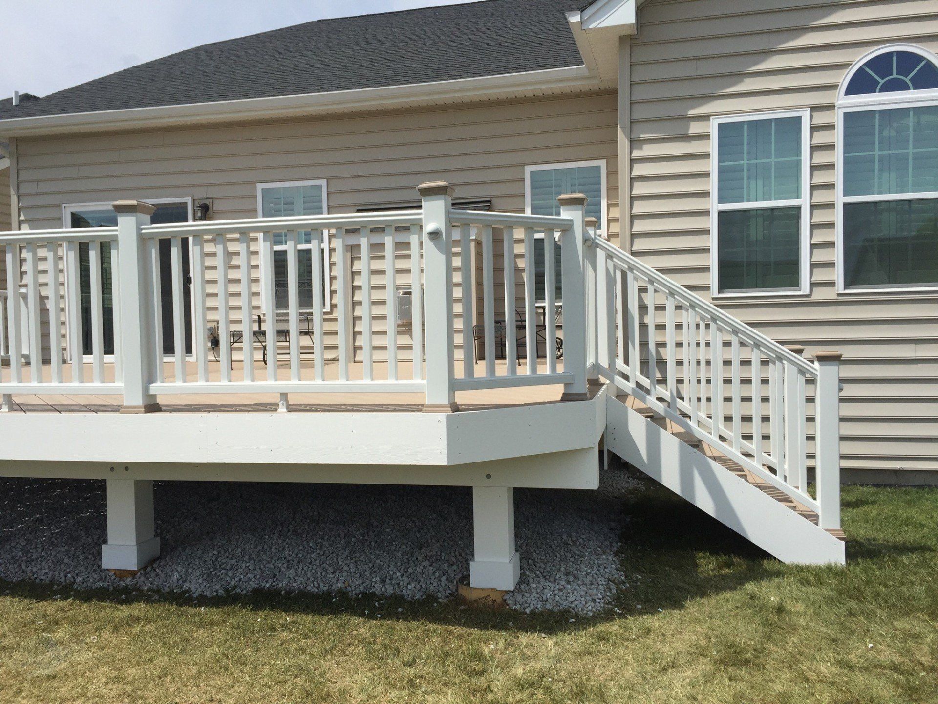 Raised wooden deck with white railing and stairs beside a beige house