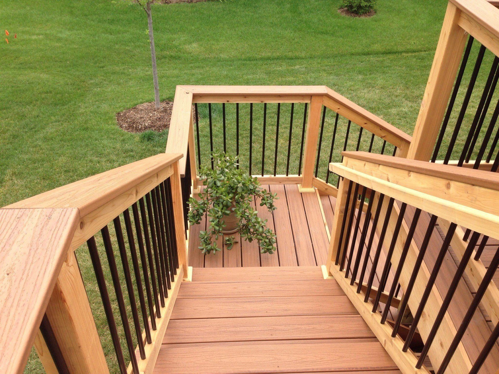Wooden deck stairs with black railings overlooking a green lawn.