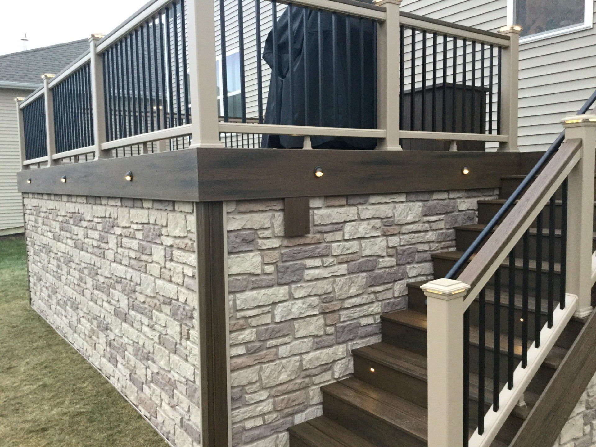 Stone-faced deck with black railing and stairs leading to a raised porch on a house