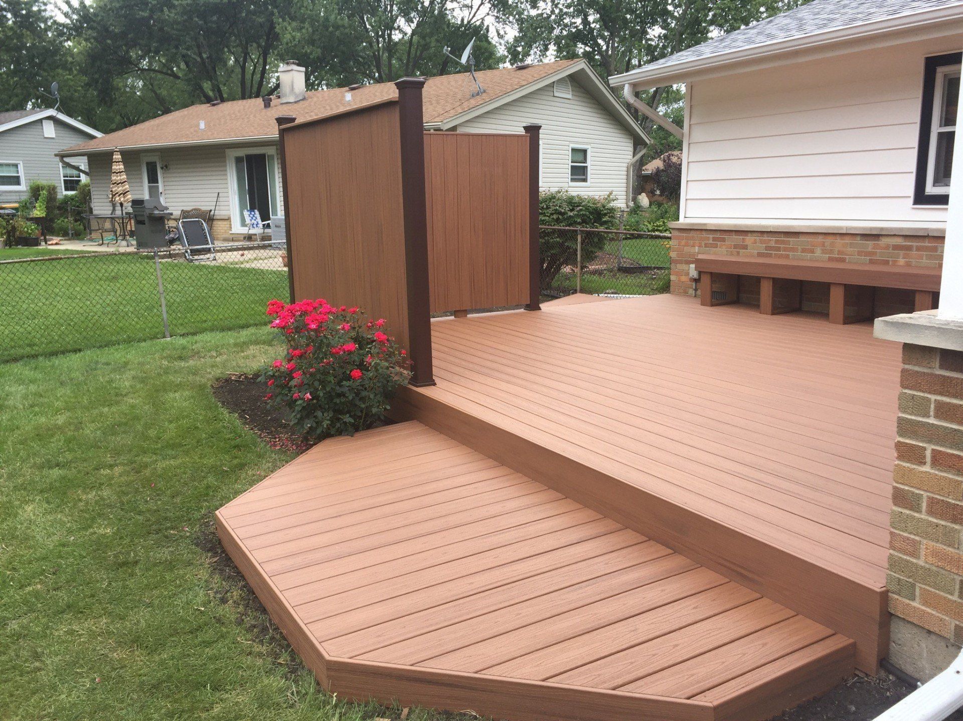 Wooden deck and steps in a backyard, with a flower bed and neighboring houses nearby