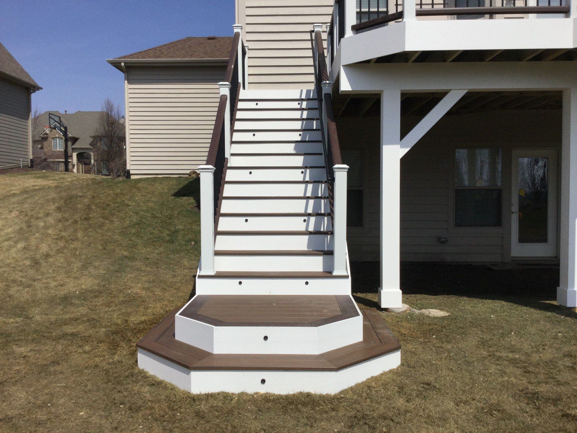 Exterior staircase with white railings leading to an elevated deck beside a house.