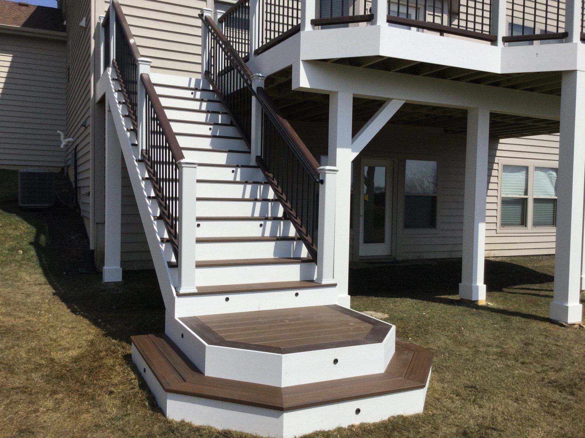 Exterior staircase with white railings leading to a raised deck above a lawn