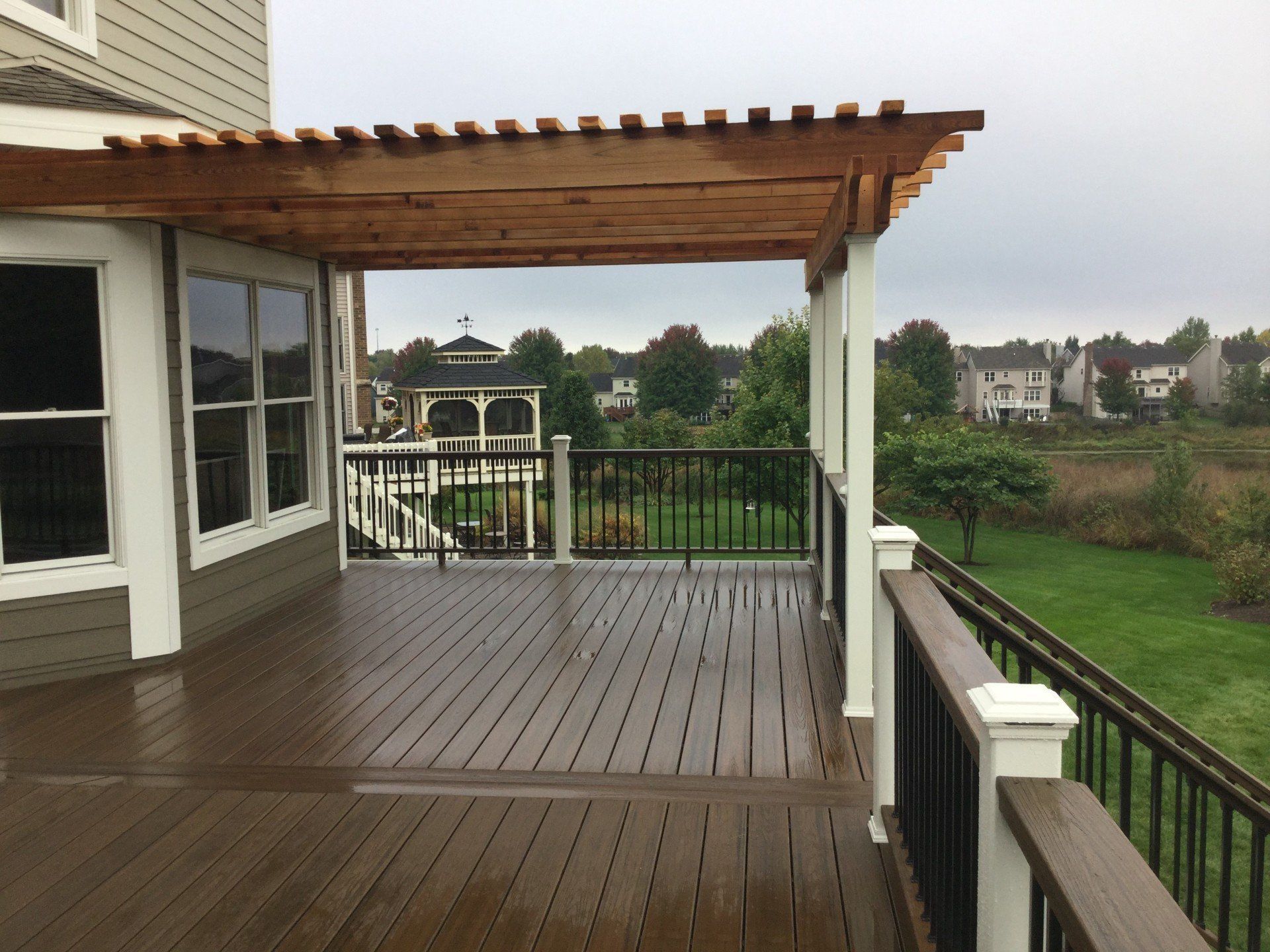 Wooden deck with pergola overlooking a green yard and neighboring houses under an overcast sky