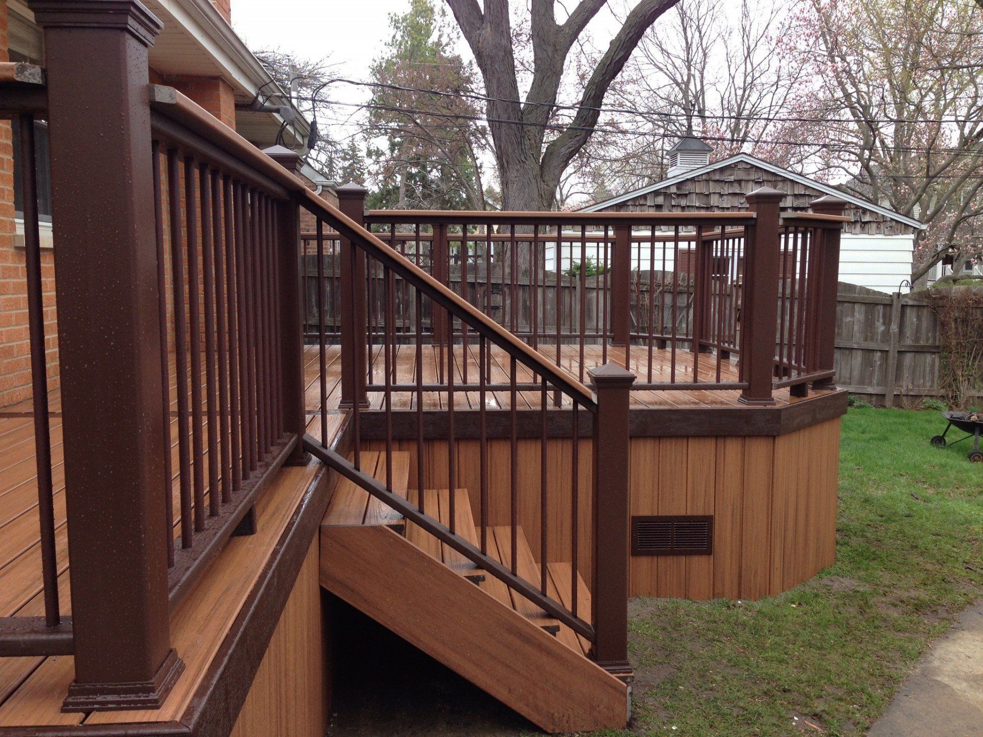 Wooden backyard deck with railings, steps, and a raised platform beside a grassy yard