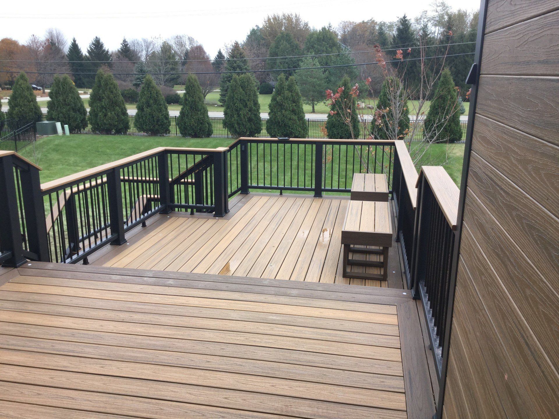 Wooden deck with black railing overlooking a grassy backyard and trees