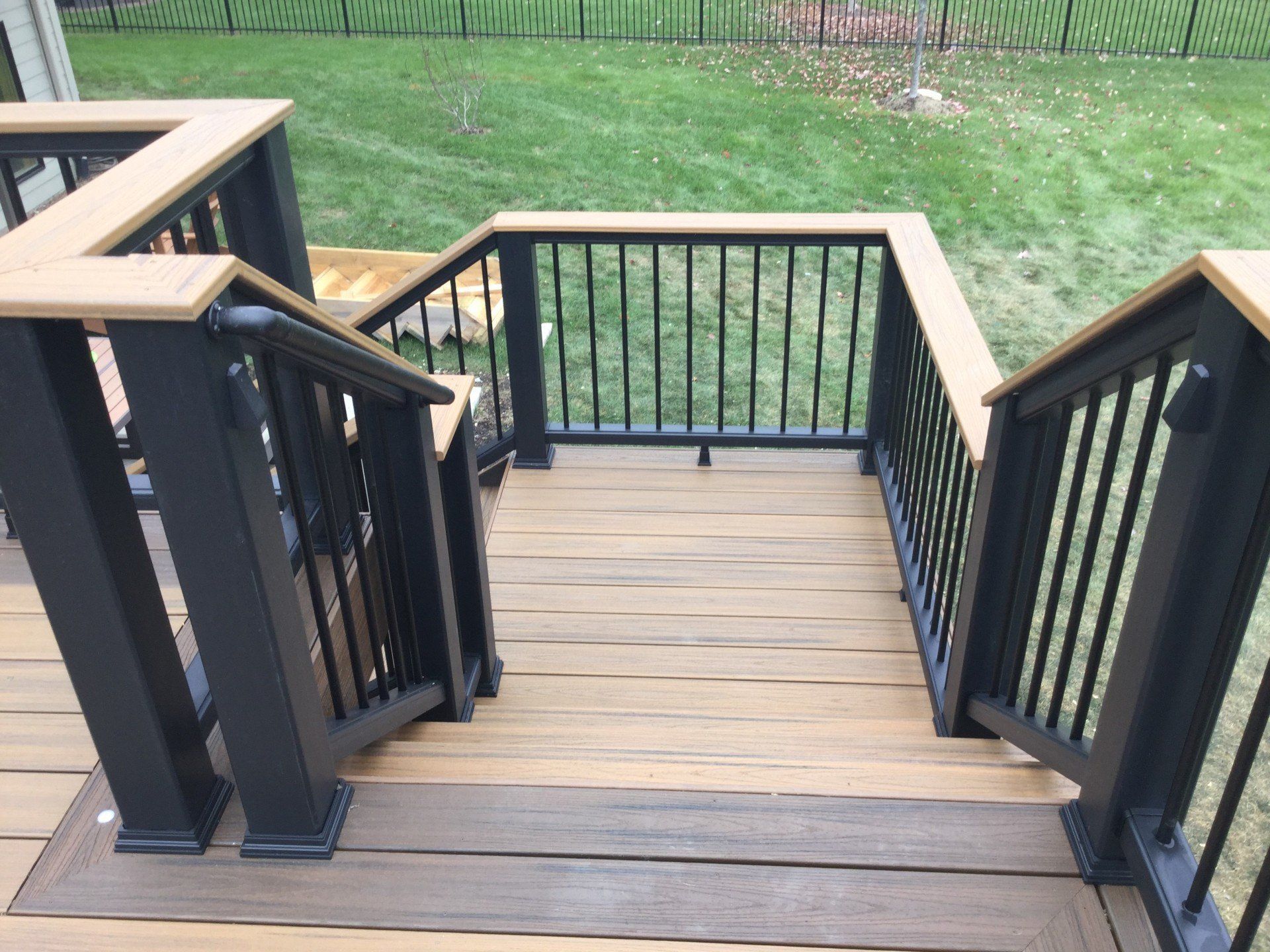 Wooden outdoor deck stairs with black railings leading down to a grassy yard