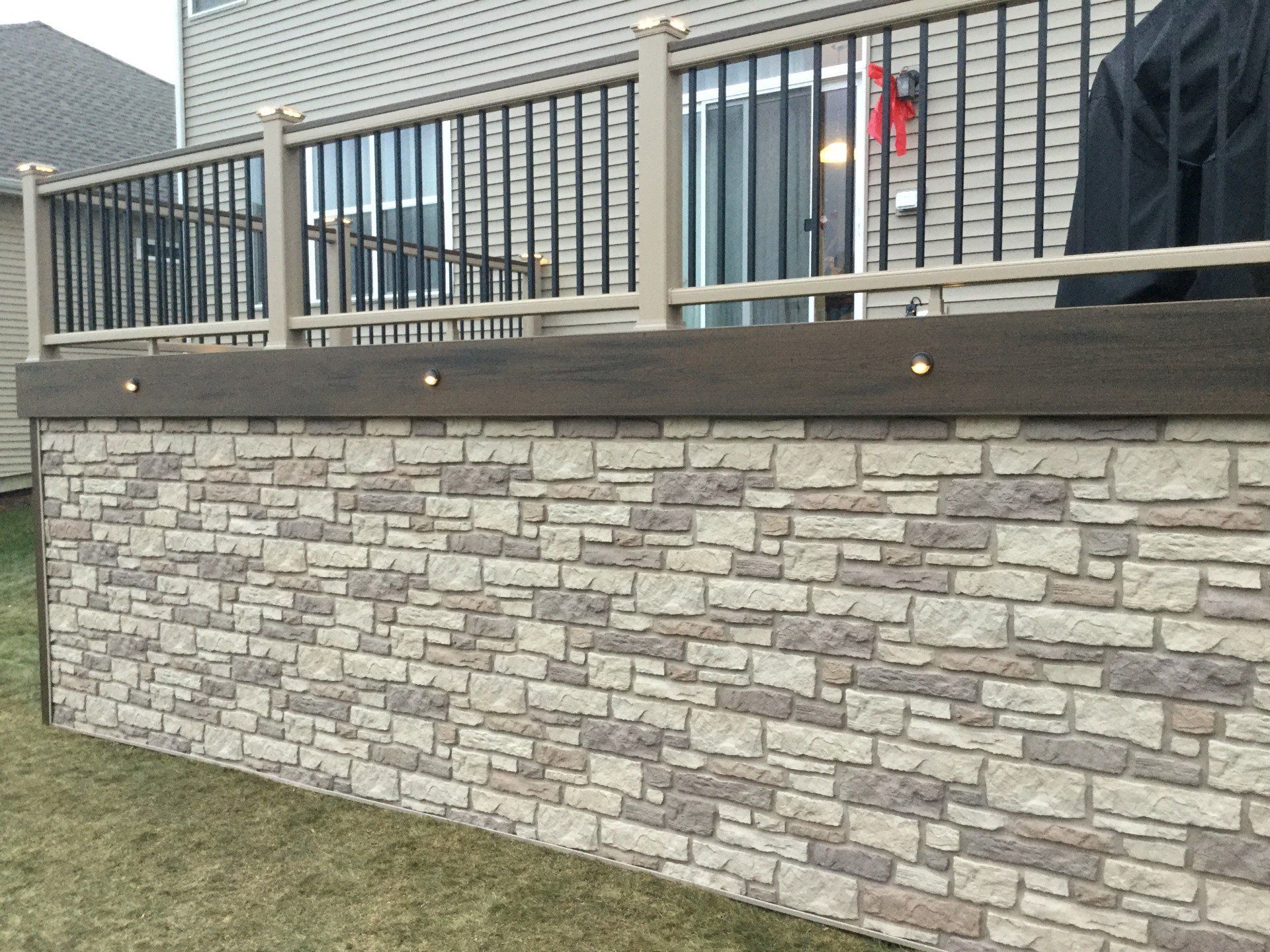 Stone retaining wall with black metal railing in front of a house deck.