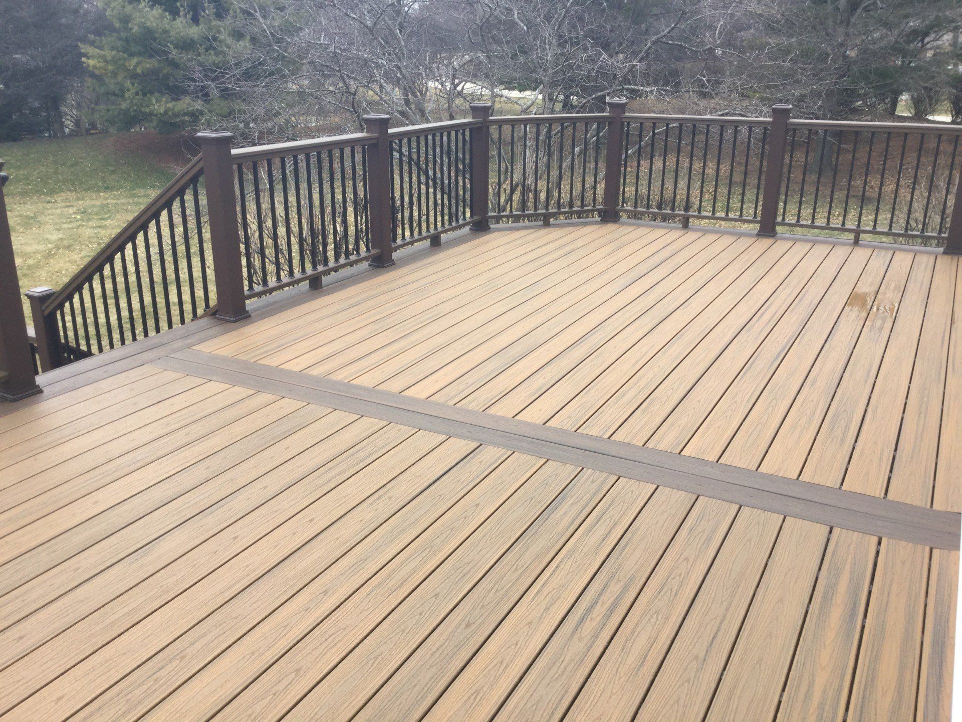 Wooden deck with black railings overlooking a grassy yard, viewed from above.