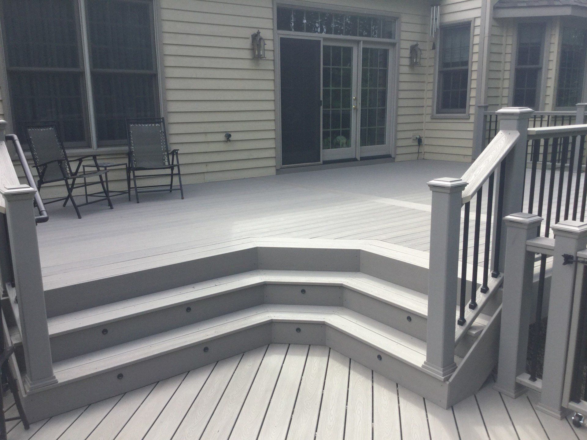 Three-tiered gray deck with white railings and sliding glass doors to a house