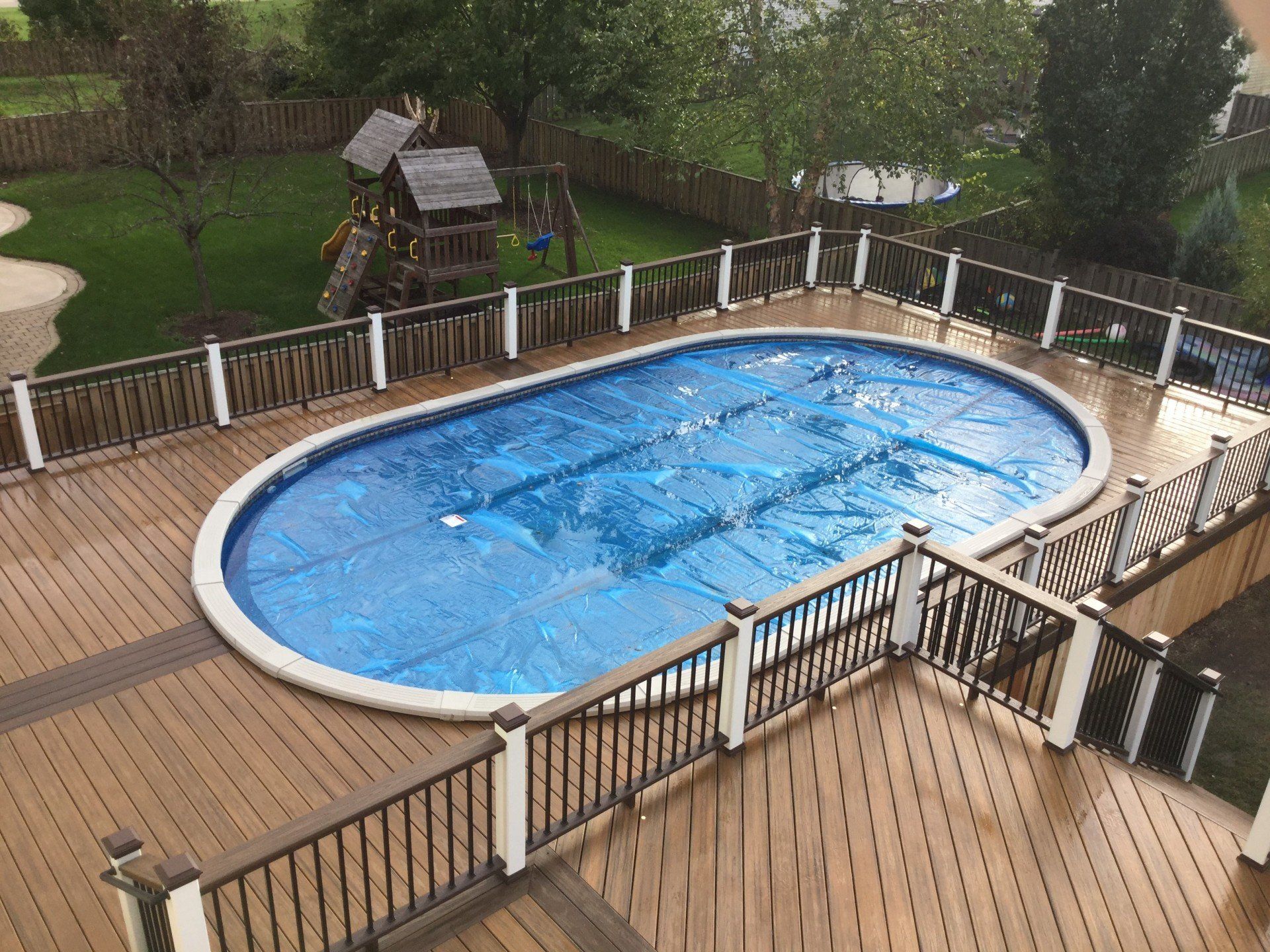 Backyard deck with an oval blue swimming pool and surrounding wooden fence