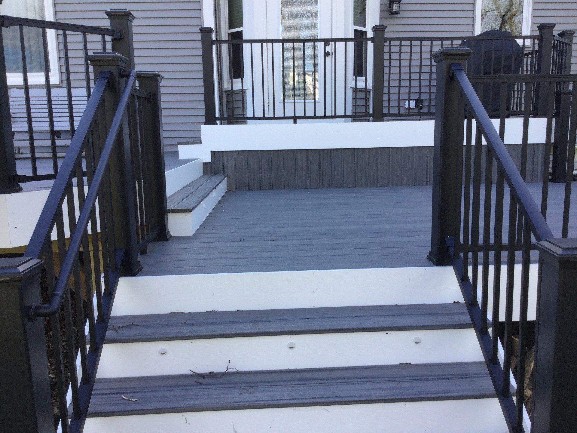 Front porch ramp with black railings and white steps leading to a gray wooden deck
