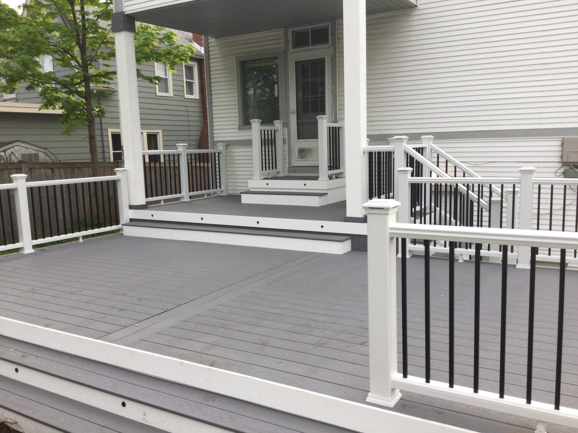 Front porch with gray composite decking, white railing, and steps leading to a white house entrance