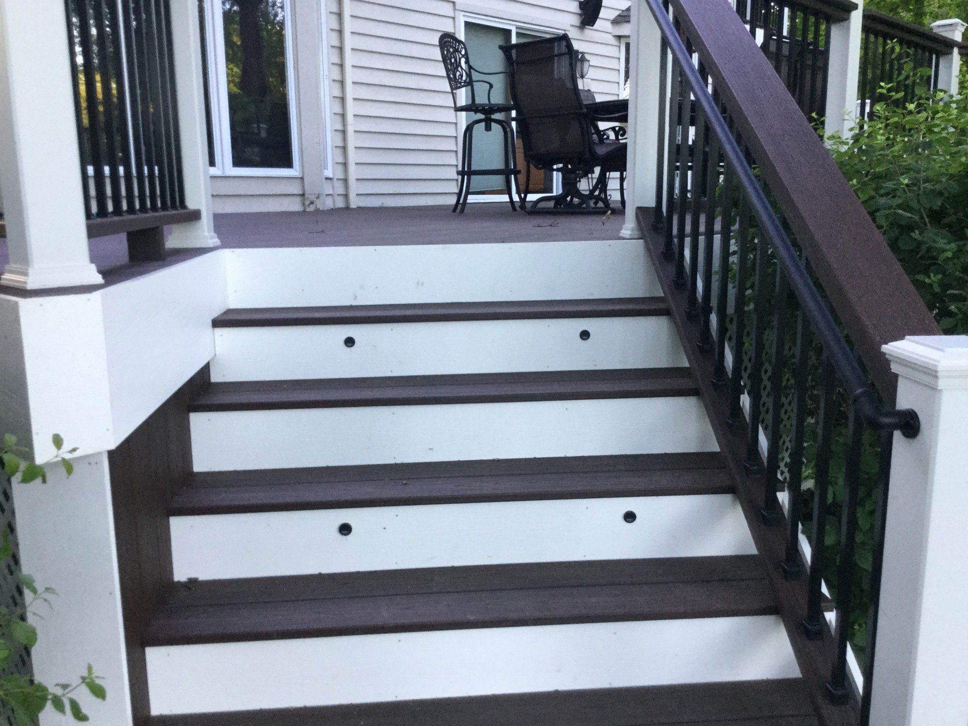Front porch steps with black railings and a small table and chairs at the top landing