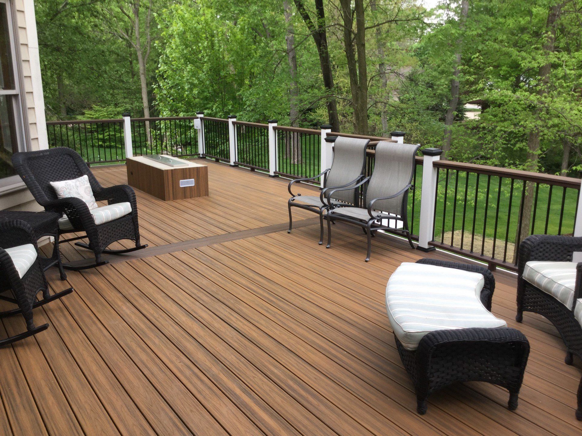 Wooden deck with wicker chairs and a bench surrounded by green trees and railing