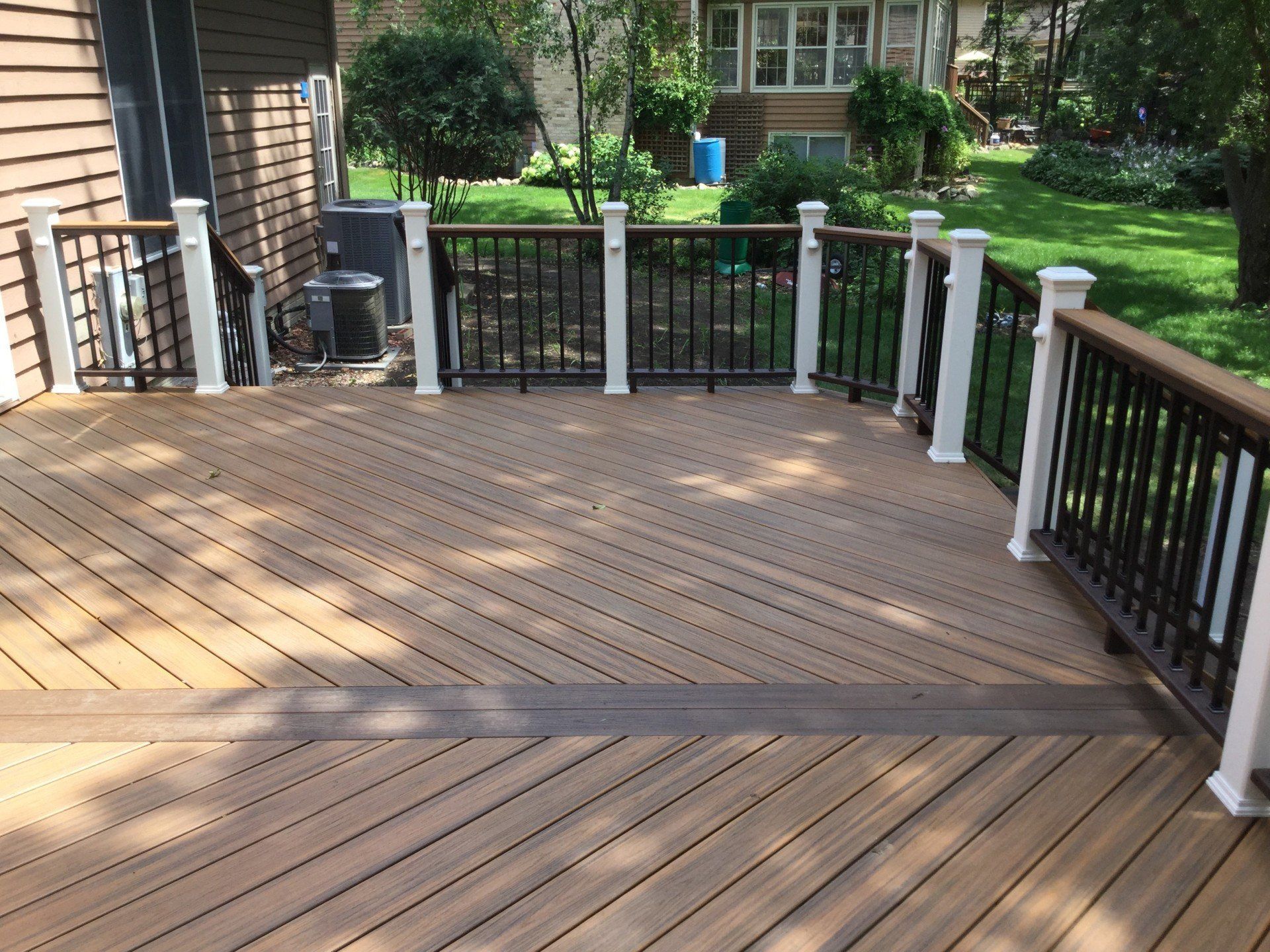 Wooden backyard deck with black railings, stairs, and a view of the green yard beyond