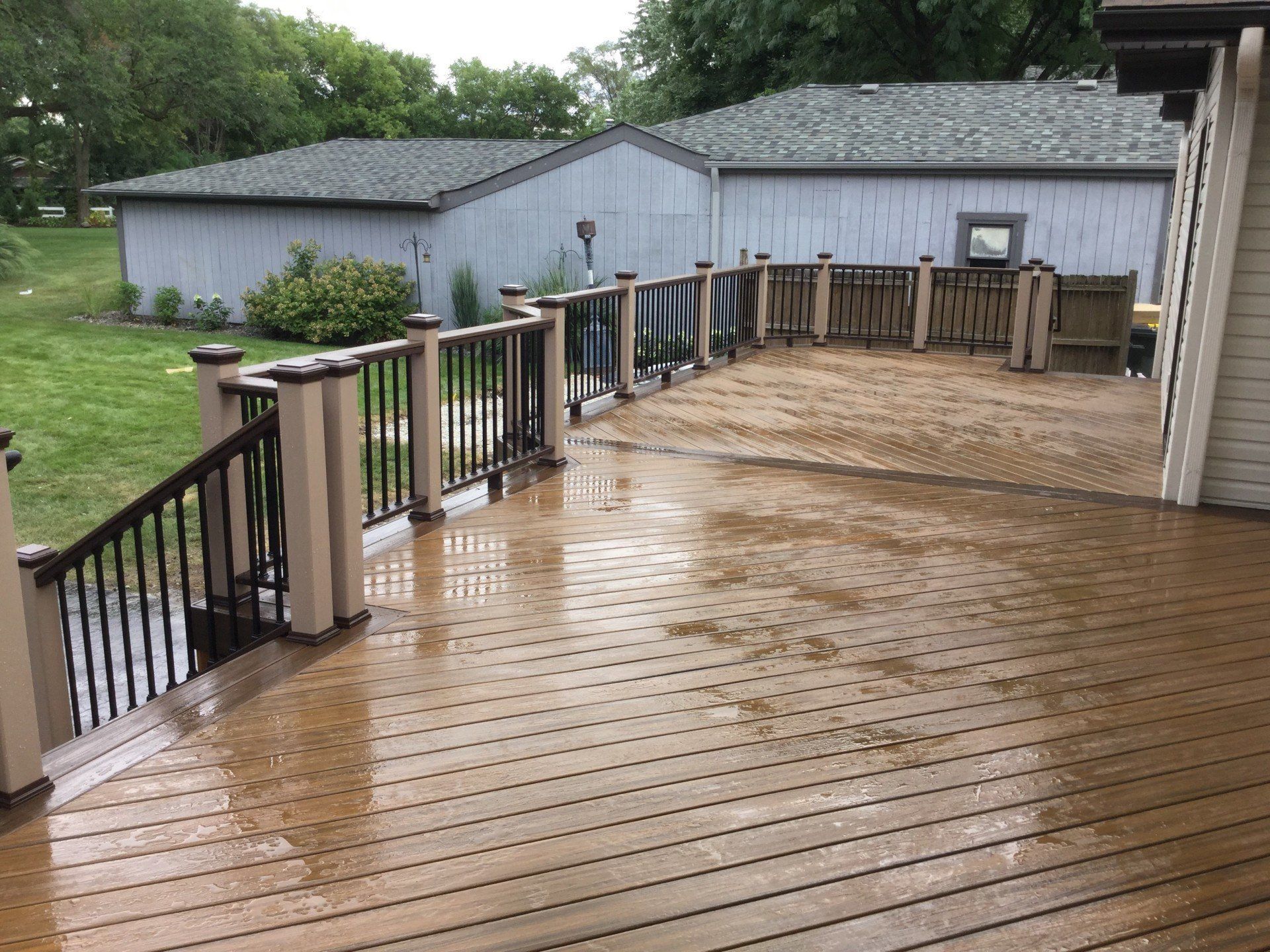 Wet wooden deck with railings beside a gray building after rain