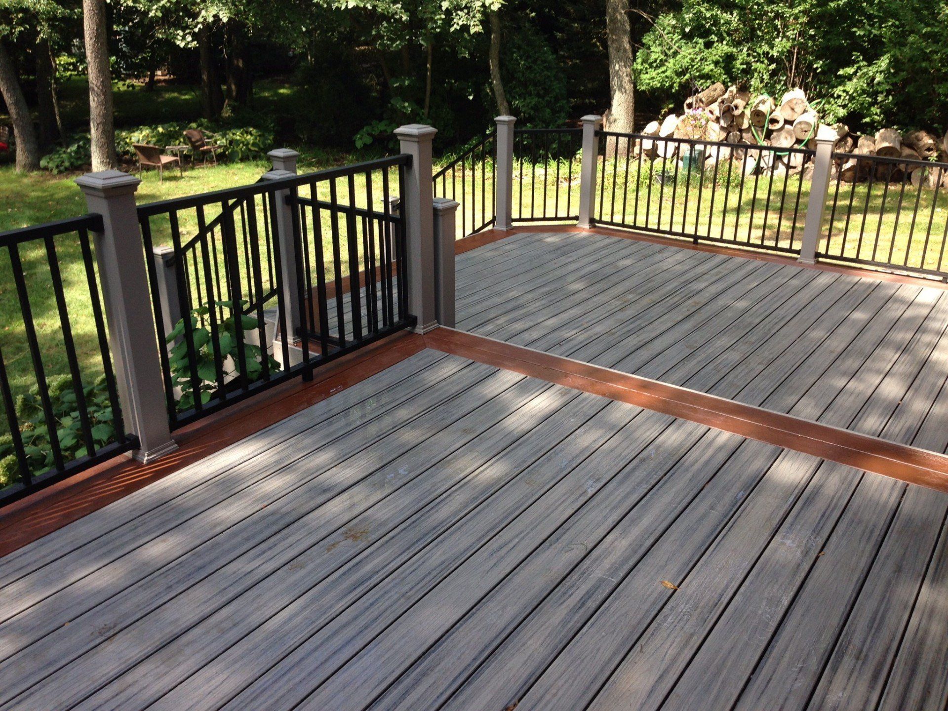 Wooden deck with black railings overlooking a green wooded yard