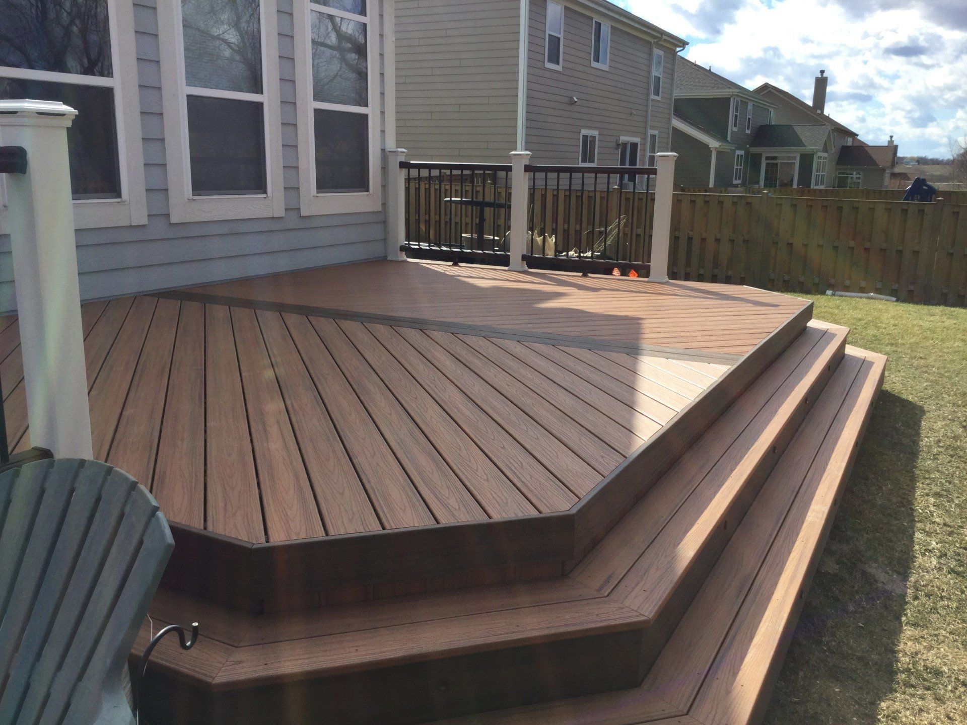 Wooden deck with steps beside a house, overlooking a fenced backyard.