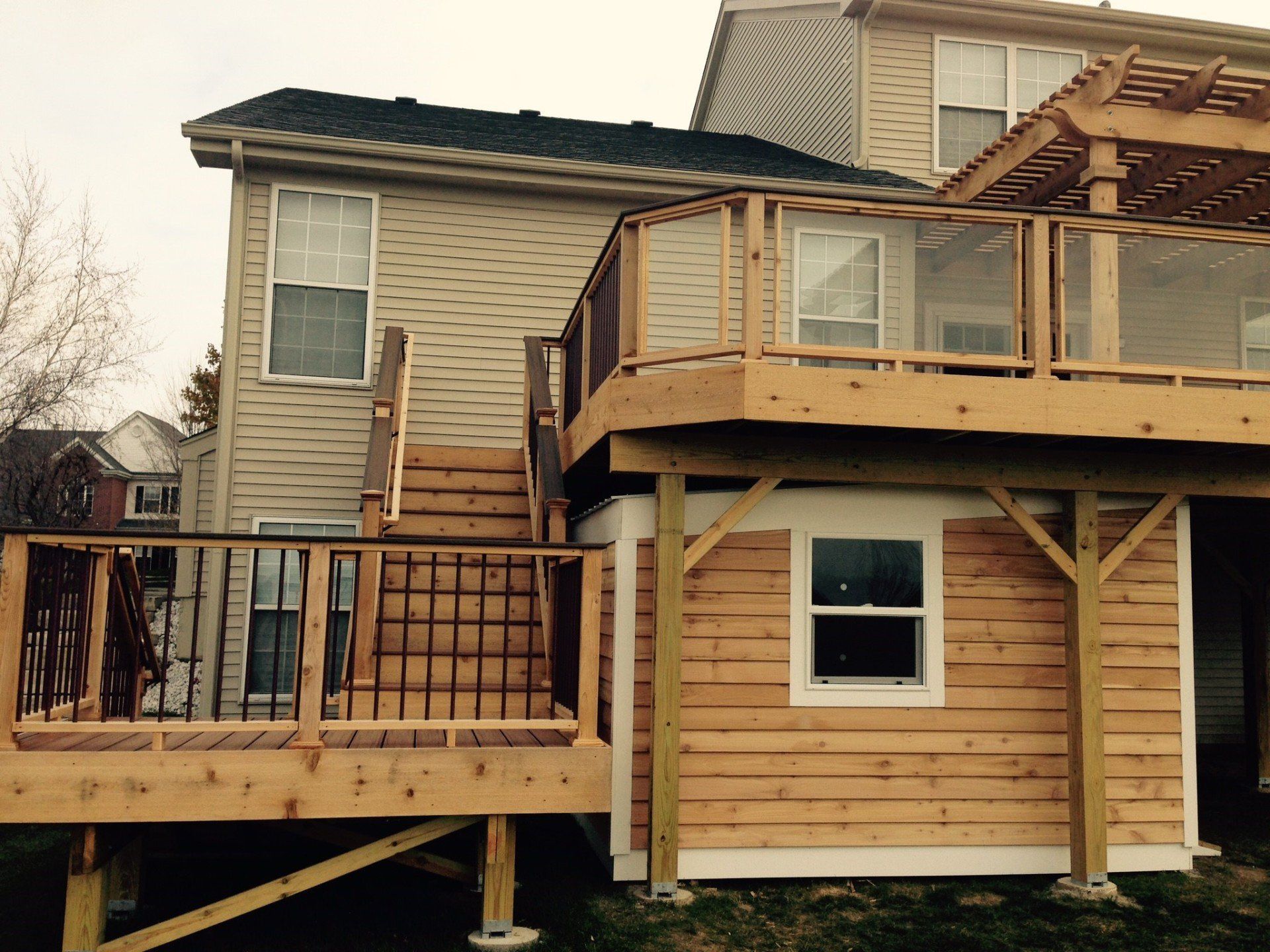 Wooden deck and balcony additions on a tan house, with black railings and a small windowed room below.