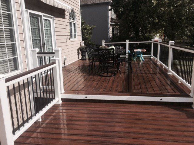 Wooden deck with black patio table and chairs beside a house, bordered by white railings
