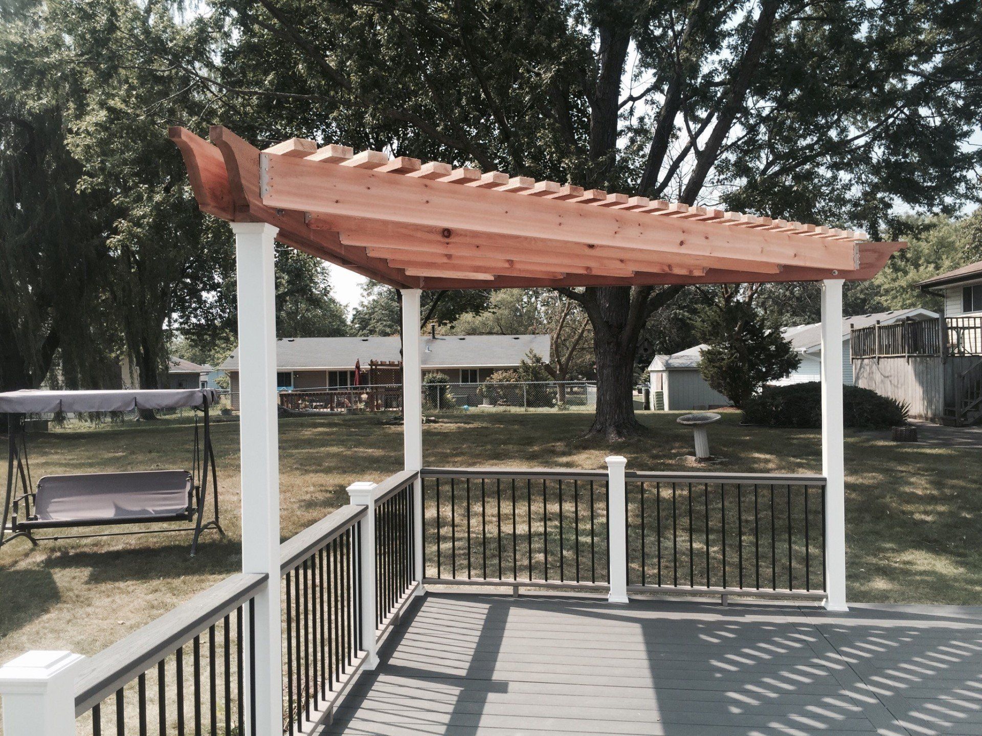 Wooden pergola over a porch deck with white railings and a yard beyond
