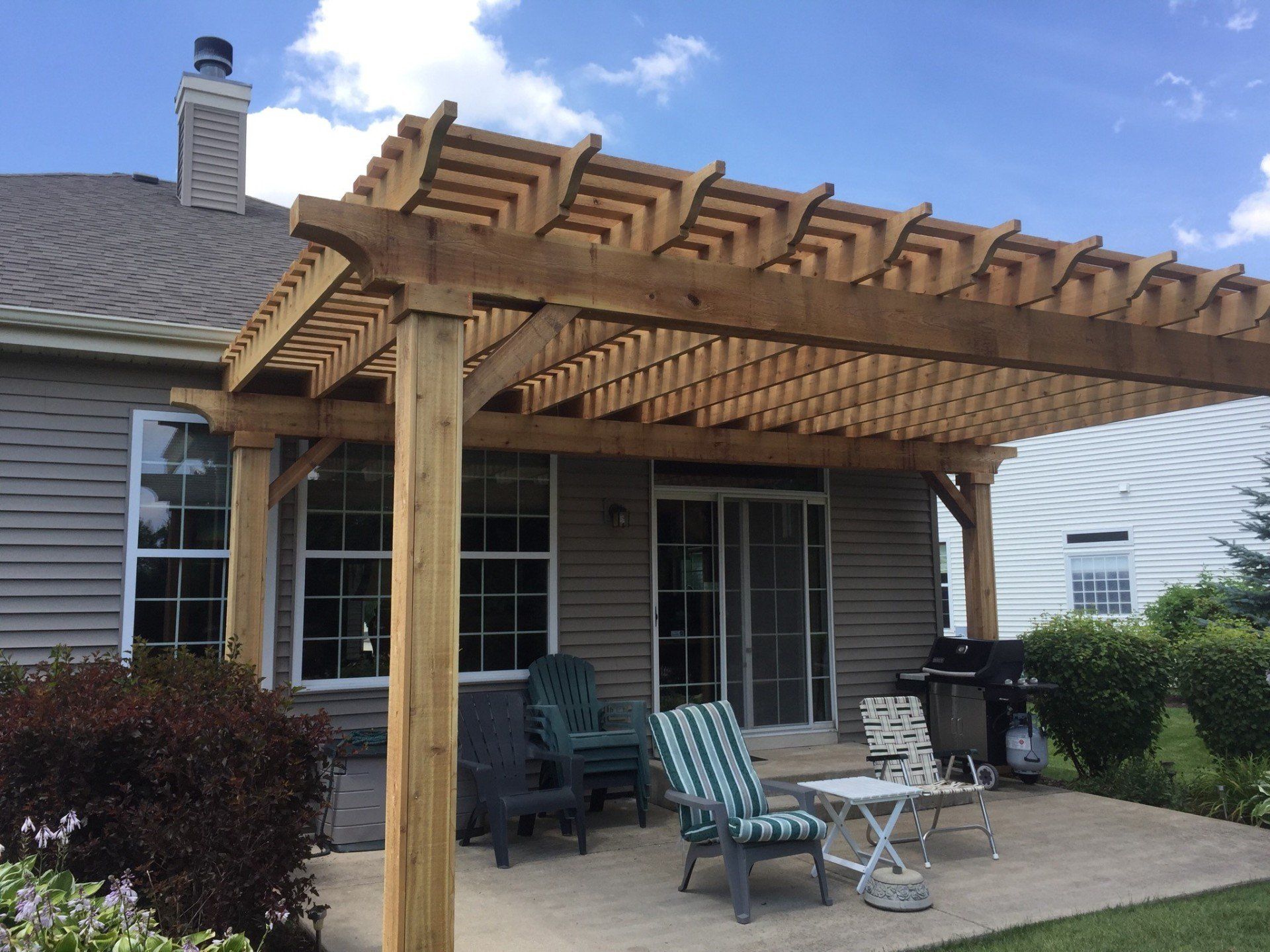 Back patio with wooden pergola, glass table and chairs, beside a brick house and sliding doors