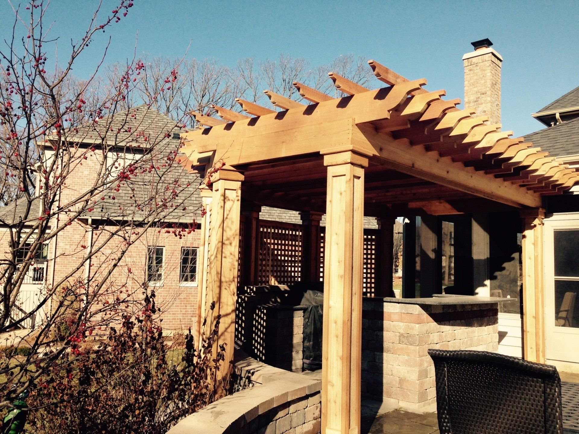Adobe-style patio pergola with wooden beams, stone columns, and a chimney beside a leafless tree