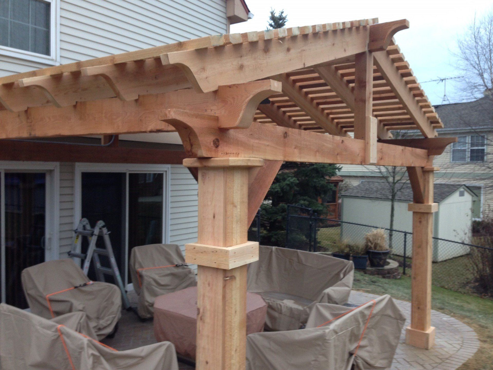 Wooden pergola over a covered patio with outdoor furniture in a suburban backyard