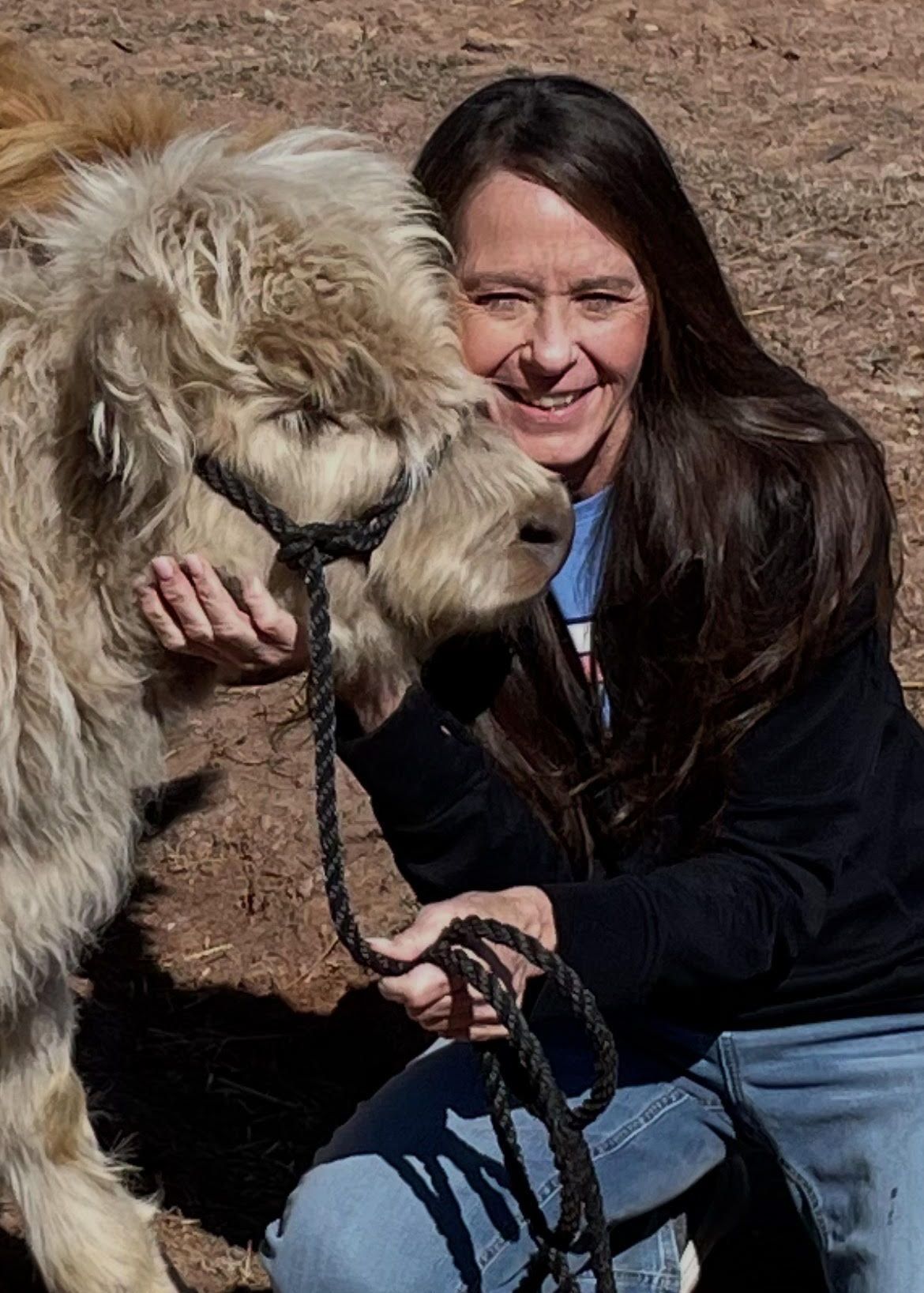 A woman is kneeling down next to a pony.
