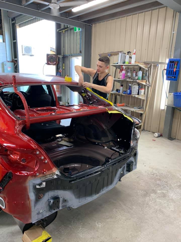 A Man is Working on a Red Car in a Garage — Arafura Crash Repairs in Darwin, NT
