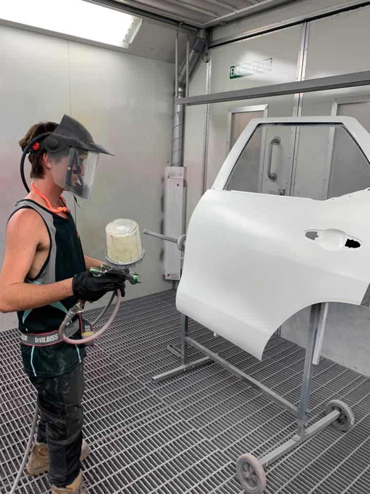 A Man is Painting a Car Door in a Paint Booth — Arafura Crash Repairs in Winnellie, NT