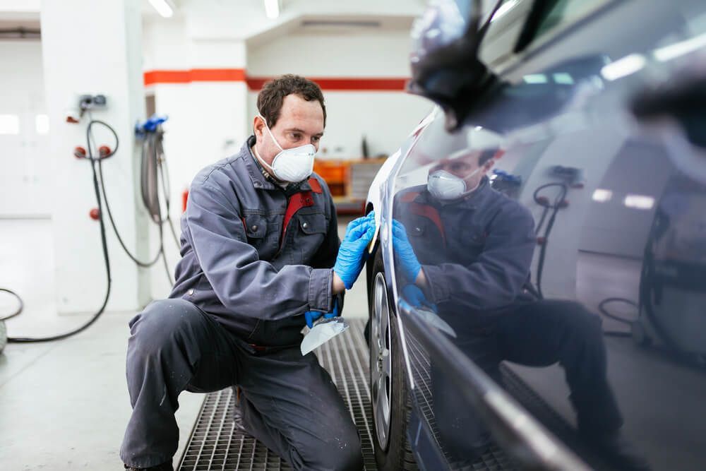 A Man Wearing a Mask and Gloves is Painting a Car in a Garage — Arafura Crash Repairs in Palmerston, NT