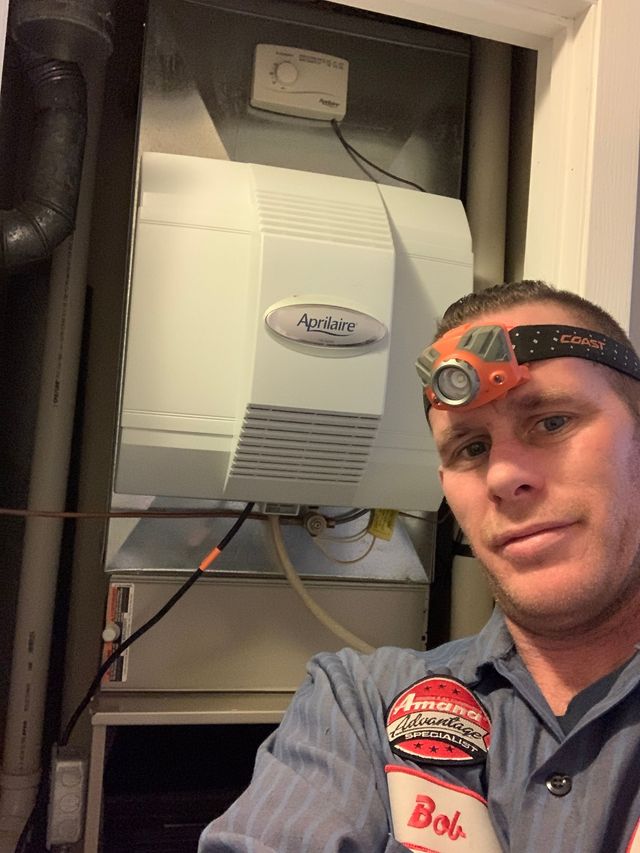 Man wearing a headlamp and work shirt beside a wall-mounted boiler in a utility closet