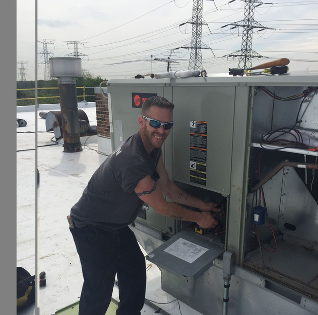 Technician working on rooftop HVAC unit with power lines in the background