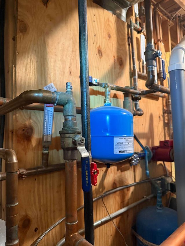 Blue water pressure tank and copper pipes in a utility room with wooden walls