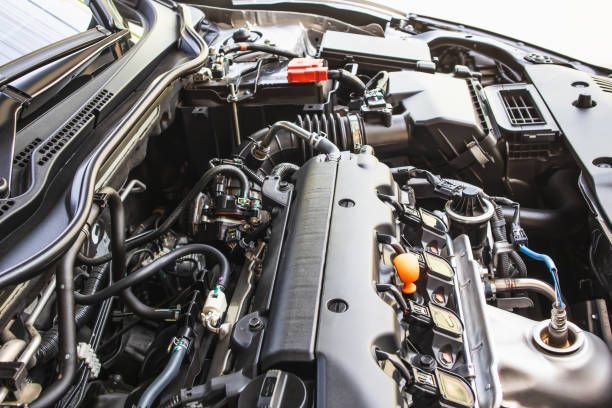 Car engine bay, black components, hoses, and orange oil cap visible.