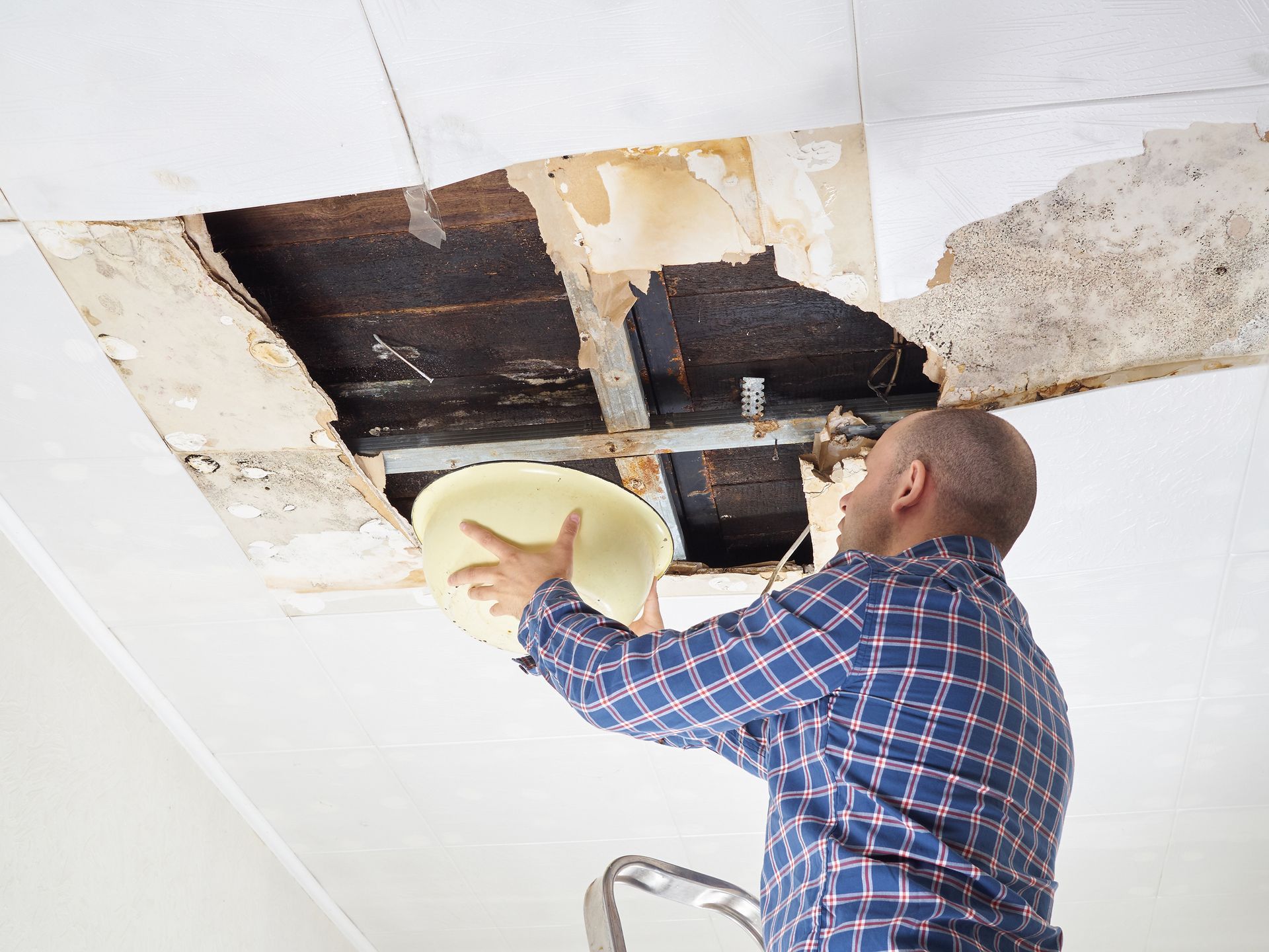 Asbestos Abatement — Hathaway Environmental in Abilene, KS A man is looking through a hole in the ceiling while holding a plate.