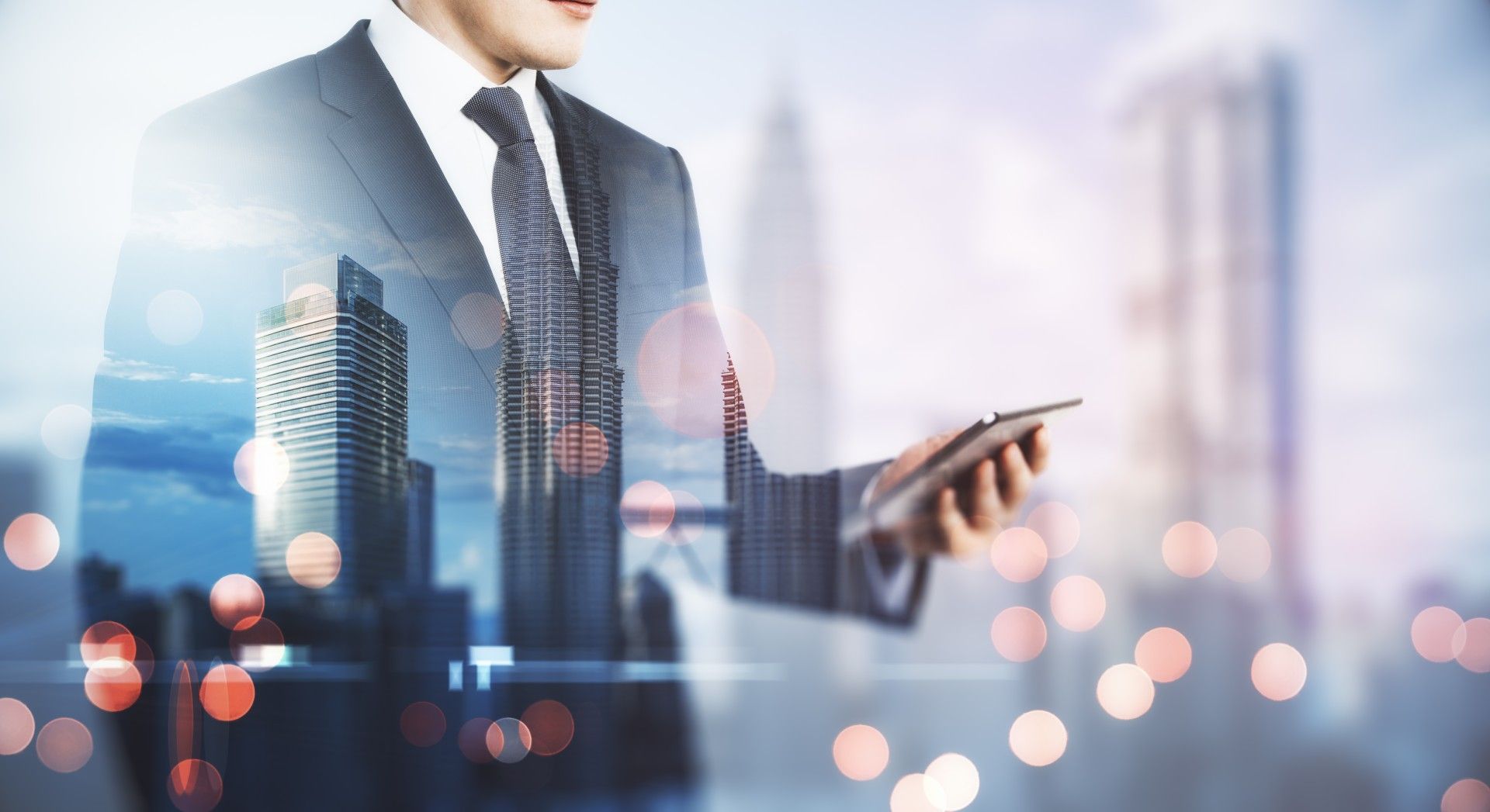 A man in a suit and tie is holding a tablet in front of a city skyline.