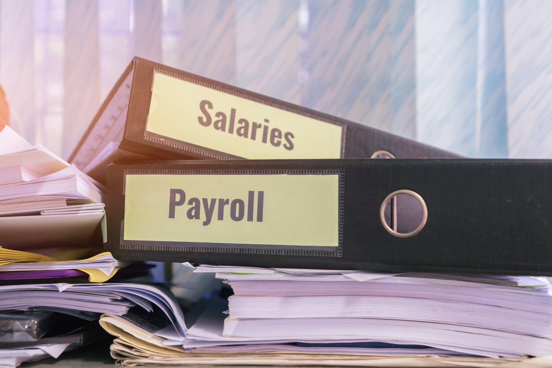 Two binders labeled salaries and payroll are stacked on top of a pile of papers.