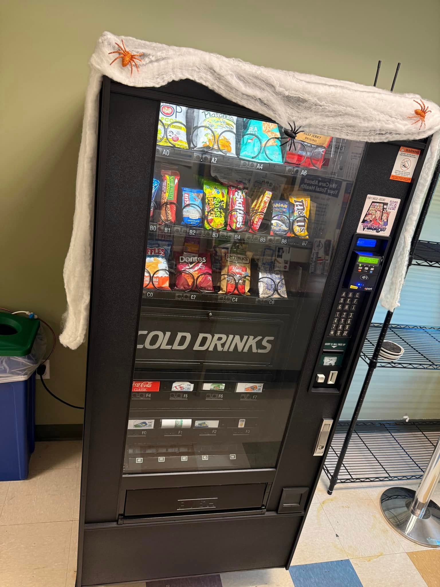 A black vending machine decorated with white spiderwebbing and toy spiders draped over the top.