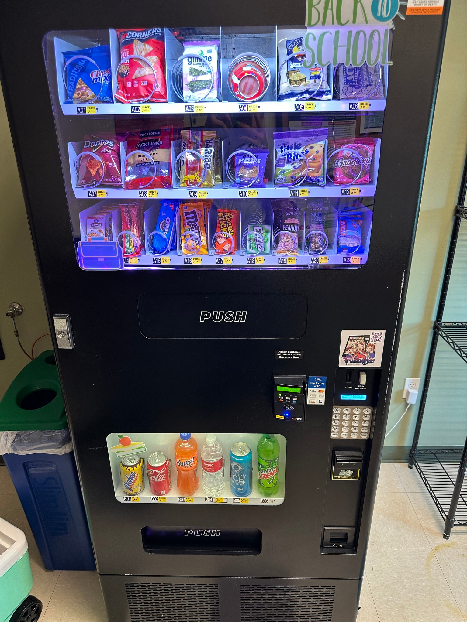 A black vending machine stocked with snacks on three top shelves and bottled beverages on the bottom shelf.