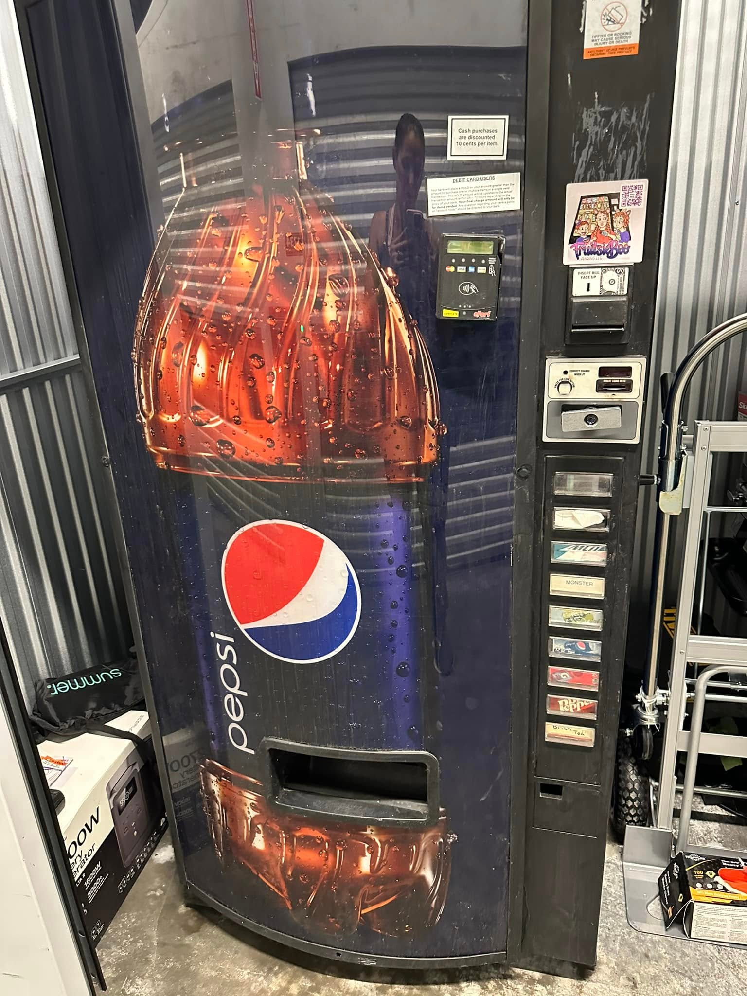 A Pepsi vending machine with a large bottle graphic on its door, positioned in a storage area.