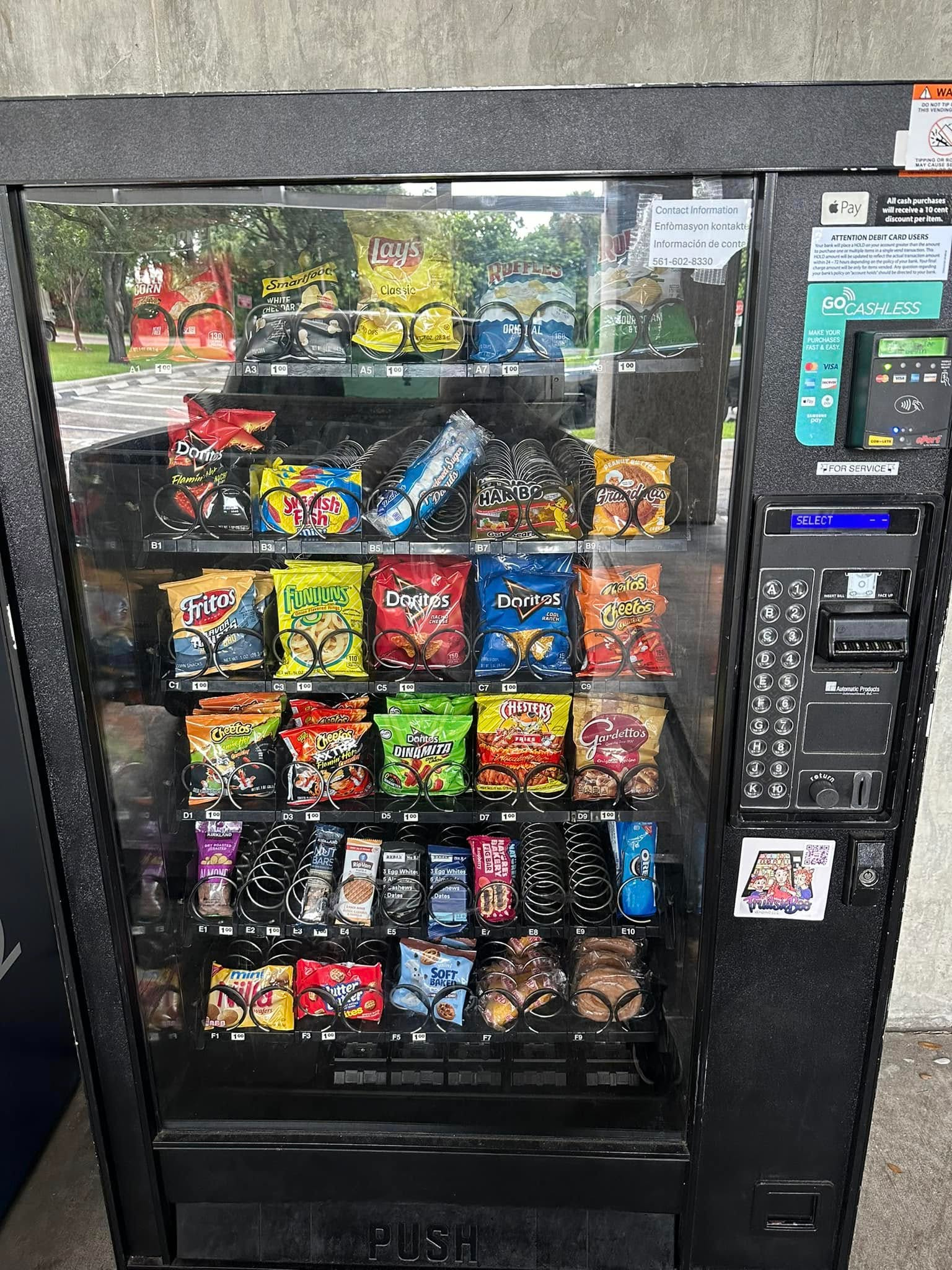 A black vending machine stocked with various snacks, chips, and candy, featuring a digital keypad and payment card reader.