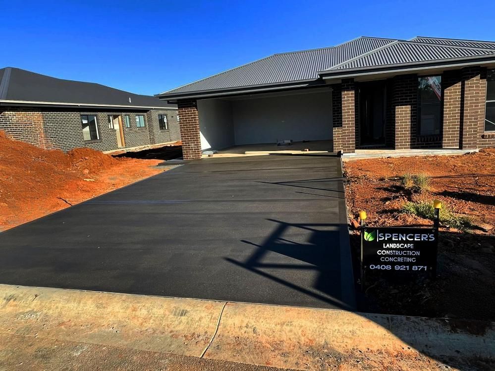 A Brick House with A Black Driveway in Front of It — Spencer's Landscape Construction & Concreting Pty Ltd in Dubbo, NSW