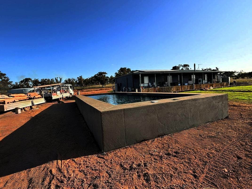 A Large Concrete Pool is in Front of a House — Spencer's Landscape Construction & Concreting Pty Ltd in Coonabarabran, NSW